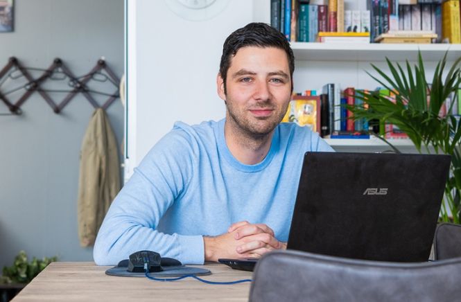 Lachende man met zijn handen gekruist achter zijn laptop