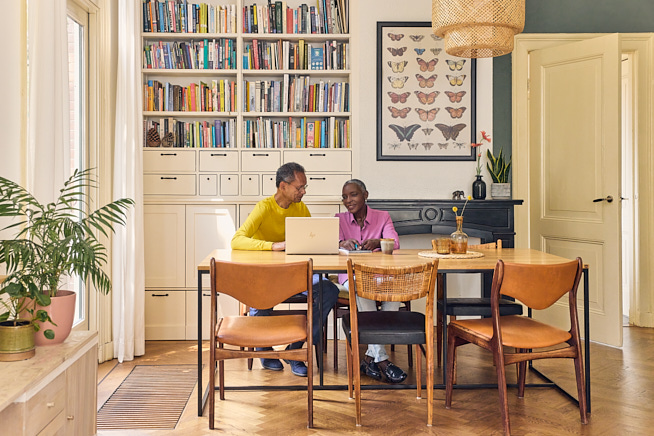 Man en vrouw zittend aan tafel in de woonkamer bezig achter een opengeklapte laptop