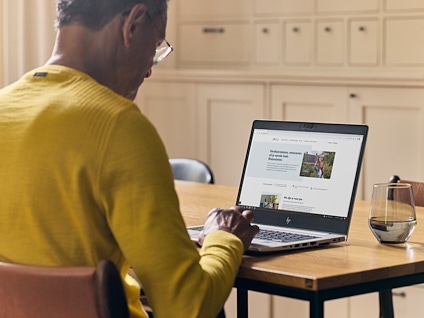 Man zittend aan tafel met een opengeklapt laptop waarop hij bezig is