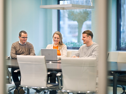 Drie mensen zittend aan een tafel achter een laptop
