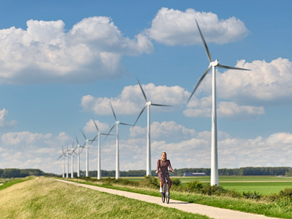 Vrouw die over een dijk fietst met windmolens op de achtergrond