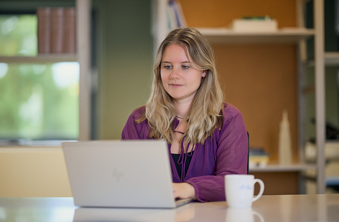 Vrouw achter haar laptop aan het werk met een koffiemok naast haar