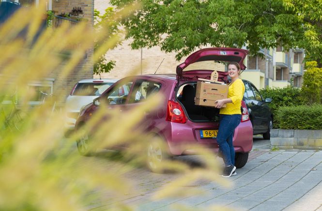 Vrouw die verhuisdoos uit openstaande auto tilt