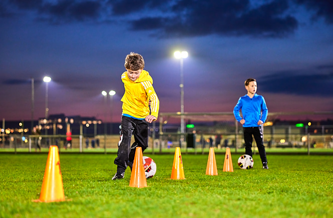 Twee voetballende jongens met de bal aan hun voet aan het slalommen tussen pionen