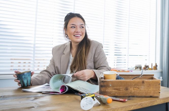 Lachende vrouw die aan tafel zit en door papieren heen bladert met een mok in haar hand