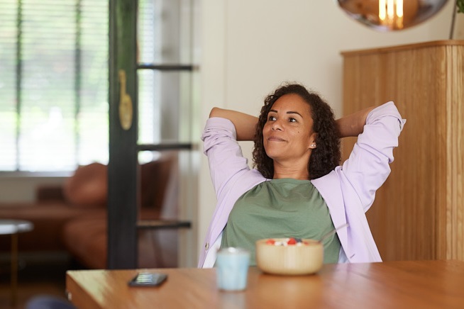 Vrouw die tevreden achterover leunt met haar handen achter haar hoofd zittend aan tafel