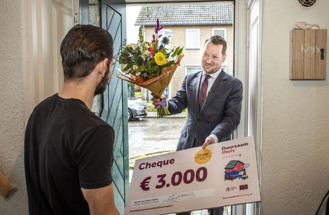 Man met cheque en bloemen in zijn handen die hij overhandigt aan een andere man