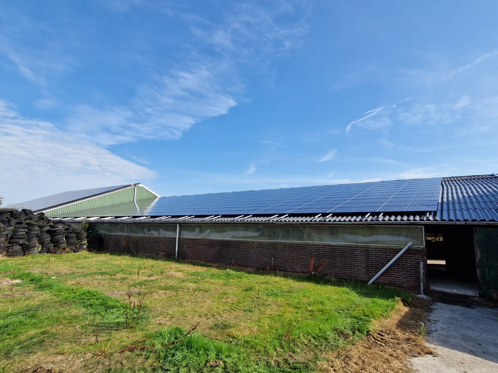 Een stal met het dak vol zonnepanelen en ervoor een grasveld