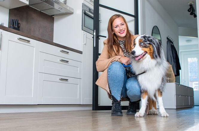 Lachende vrouw hurkend naast haar hond in de keuken