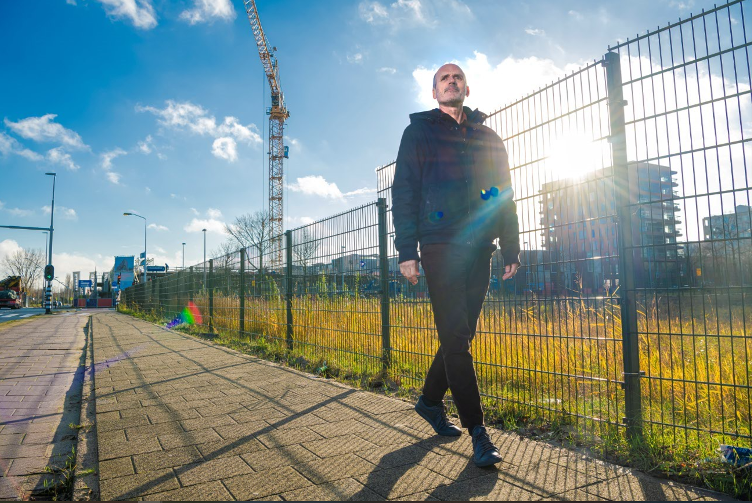 Man lopend langs een hek met op de achtergrond een hijskraan en het Transformatie terrein Poppies